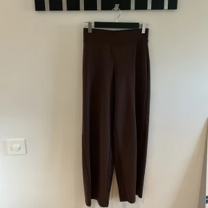 Bruna byxor - Ett par bruna byxor med hög midja och vida ben. Byxorna har en enkel och stilren design utan synliga detaljer som knappar eller dragkedjor.