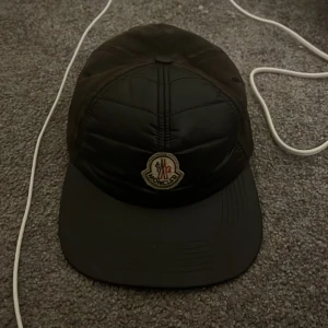 Svart keps från Moncler - En svart keps från Moncler med en broderad logotyp på framsidan.  Justerbar rem på baksidan. Använd ganska mycket men ändå fräsch. Skriv för mer bilder!