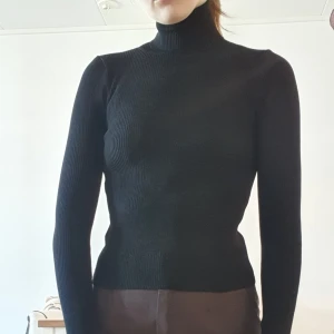 Svart, ribbad, polotröja - Svart, ribbad, polotröja med lite "skav" längst ner på tröjan (bild 3). Med lång krage som går att vika ner typ 3 ggr. Ganska tajt. 