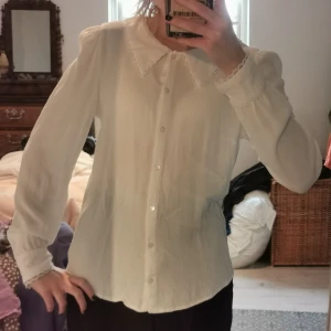 Fin skjorta/blus med spets  - Fin skjorta/blus med spetskant runt krage och ärmar. Lite osäker på vilket material det är men tror viskos. Fin att göra layers med typ under väst eller klänning när det är kallt! 