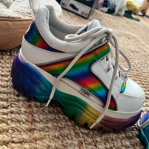 Buffalo London Rainbow - Vita Buffaloes med regnbågsfärger på sidorna och sulan.  Finns några mindre skador men överlag är skorna i bra skick.  Storlek 39 