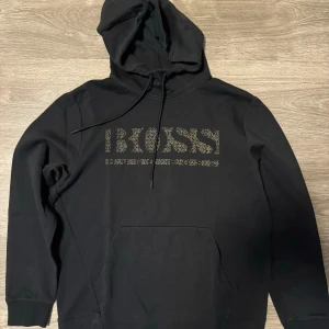 Svart BOSS hoodie med logo, storlek M - Säljer en svart BOSS hoodie i storlek M med en framträdande BOSS-logo på bröstet. Hoodien är i mycket bra skick och har en bekväm passform
