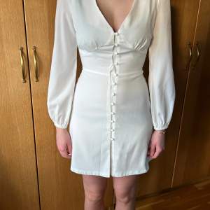 Snygg vit klänning med lång ärm och fina detaljer från Nelly X Glamourous, strl 34, är i mycket fint skick, endast använd ett par gånger. Perfekt till avslutningen, student eller sommaren!