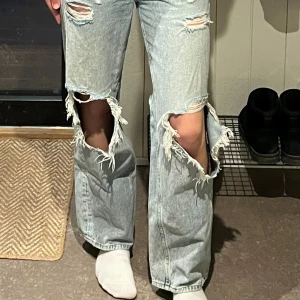 Jeans - Ljusblåa jeans i storlek 38. Skulle säga att de är mid-waist och modellen är baggy (Loose-straight) med ganska stora hål vid knäna, som ger en ganska street-ig look. De är köpta second hand så vet tyvärr inte vart de är ifrån. Sparsamt använda