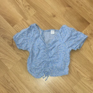 Tröja - Tröjan är ljus blå och har vita blommor på. Med en roset på.