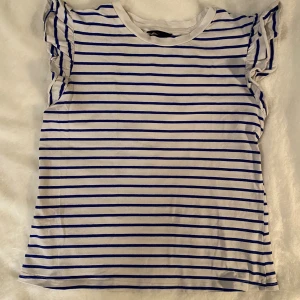 Vit topp med blåa ränder i strl s - Vit topp med blåa ränder i strl s.  Mått Över axeln: ca 35 cm Längd från axeln och ner: ca 53 cm  Använd men i bra begagnat skick.  Kommer från ett djur och rökfritt hem.