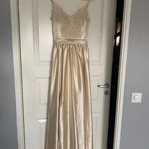 Balklänning - Champagnefärgad balklänning i satin. Köpte den av en tjej som använt den två gånger tidigare, jättefint skick! Står ingen strolek men passar en s. 