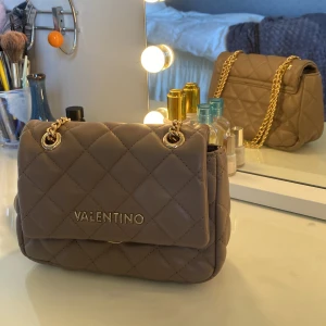 Äkta valentino väska  -  Äkta beige valentino väska i fint skick. En liten defekt finns på valentino loggan där guld färgen gått bort lite, men annars ser väskan ut som ny! Finns även bra förvaring inuti den.💞💞  Mått: Höjd: 13cm  Längd: 19cm  Djup: 5/6cm 