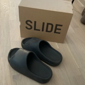 Yeezy slide  - Jag säljer ett par yeezy slides onyx eftersom att dem har blivit för små. De är i ett väldigt bra skick 8/10. Den ända defekten är undersidan på ena sliden men varken syns eller märks när man använder de. Perfekta nu till sommaren. Kvitto finns. 