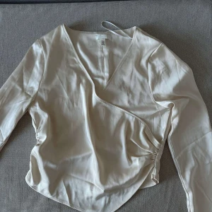 Vit topp - En jättefin gräddvit omlottopp i typ sidentyg, från h&m. Bra skick. Slitsen på ärmarna gör en såå fin detalj! Storlek M