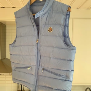 Moncler väst (kvitto finns) - Nu dags att sälja min ljusblå Moncler Gui-väst i storlek 2/M. Tyvärr har den blivit för liten för mig. Västen är i toppskick 9/10, och har bara använts sparsamt.  Vid minsta fundering eller om du vill ha fler bilder, tveka inte att höra av dig.  