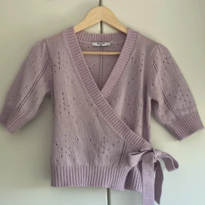 Stickad tröja - Super söt stickad kortärmad tröja med omlott knytning. Den är i en ljus lila/rosa färg och har puffärmar. Ny pris 449 kr från NA-KD 🌸