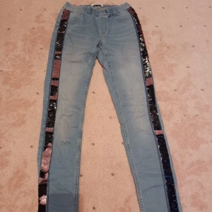 Blåa jeans med svart och rosa glitter på sidorna - Säljer nu dessa coola och unika jeans som är blå med paljetter på sidorna som är svarta och rosa. De är sparsamt använda och därför i bra skick. Storleken är 164 men passar också xs 