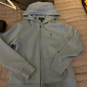 Ljus blå polo zip hoodie storlek L i barn size (14-16 år)  Säljer på grund av att den aldrig används  Ny pris 1000 från kidsbrandstore 