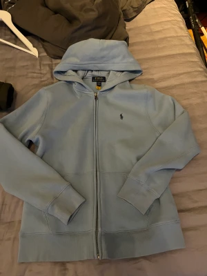Polo zip - Ljus blå polo zip hoodie storlek L i barn size (14-16 år)  Säljer på grund av att den aldrig används  Ny pris 1000 från kidsbrandstore 