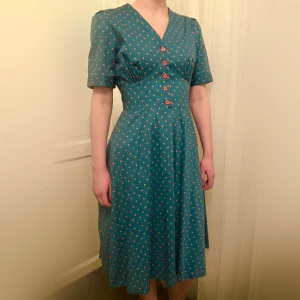 Prickig turkos retroklänning - Jag älskar den här klänningen så mycket, den har jättefina detaljer på överdelen vid bysten och små knappar. Den har också band vid rycken som låter en att anpassa storleken lite med en fin rosett på baksidan. Jättebra skick 