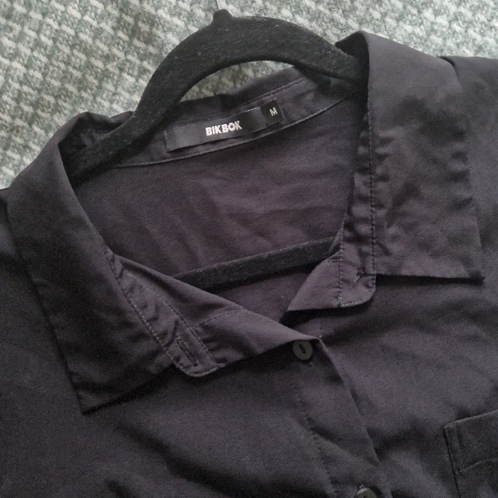 En svart kortärmad skjorta, använd någon enstaka gång. En bröstficka och detalj i ryggen. Avslappnad passform. Tunn polyester, ej stretchig.. Skjortor.