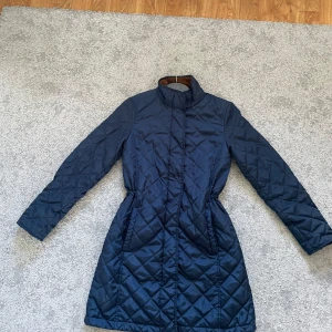 Blå lång vinterridjacka  - Vinterridjacka: CRW  Skick: Använd en hel vinter, sparsamt använd. Inga defekter  Storlek: Passar ålder 10-14, XS. Får plats med ridväst under Öppning baktill så praktiskt att rida med. Håller värmen bra även fast den är lite tunn. Bekväm och skön.