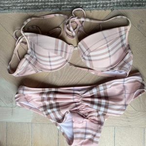 Burberry bikini rosa S - Äkta vintage burberry bikini i ljusrosa och beige i klassiska mönstret. Toppen är storlek S och känns som en S. Nederdelen är i storlek XL men passar mig som är S. Jag har sytt dit scrunchen för att den ska sitta snyggare där bak. 