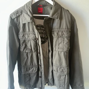 Safarijacka S.Oliver - Galet snygg safarijacka från S.Oliver. Storlek L. Modellen på bilden är 183 cm lång och väger 72 kg. Inga tecken på användning - inga defekter. Pris 499.