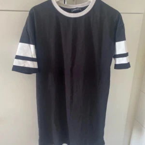 Svart t-shirt med vita detaljer - En svart t-shirt med vita detaljer på ärmarna. T-shirten har korta ärmar och en rund halsringning.