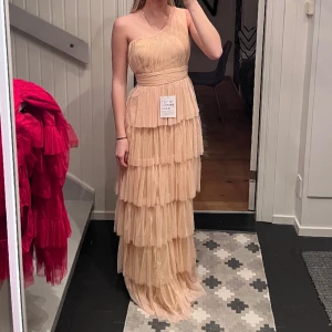 Balklänning med volanger - Säljer en helt oanvänd superfin balklänning med volanger. Alla lappar sitter på och den är endast provad 1 gång. Färgen framgår inte helt på mina egna bilder, som man ser på modellbilderna så är den mer åt det rosa hållet i verkligheten! ❣️