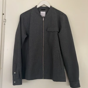 Tunn jacka från LINDBERGH - Tunn jacka från Lindbergh i mycket bra skick, i storlek Medium! Den har en fin grå färg och funkar bra att ha inomhus på vintern men även som en jacka på vår/sommar.