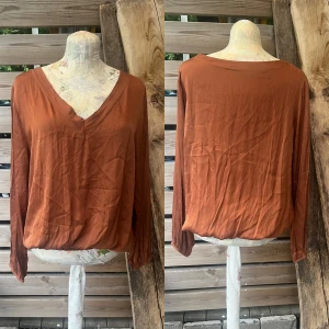 Så fin glansig blus i viskos/siden från Made in italy  - Super härlig skön blus med v-ringning, resår nedtill samt i ärmslutet. Så fin passform! Går att antingen ha resåren i midjan, el dra ned den på höften. Stl M, viskos/siden/elastan. Pytte tråddragning bak vid nacken, sista bilden. Rostfärgad