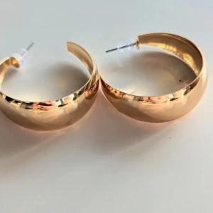 Guldörhängen i halvmåneform - Ett par eleganta örhängen i guld med en halvmåneform. Örhängena har en blank yta och är utrustade med plaststopp för att hålla dem säkert på plats.