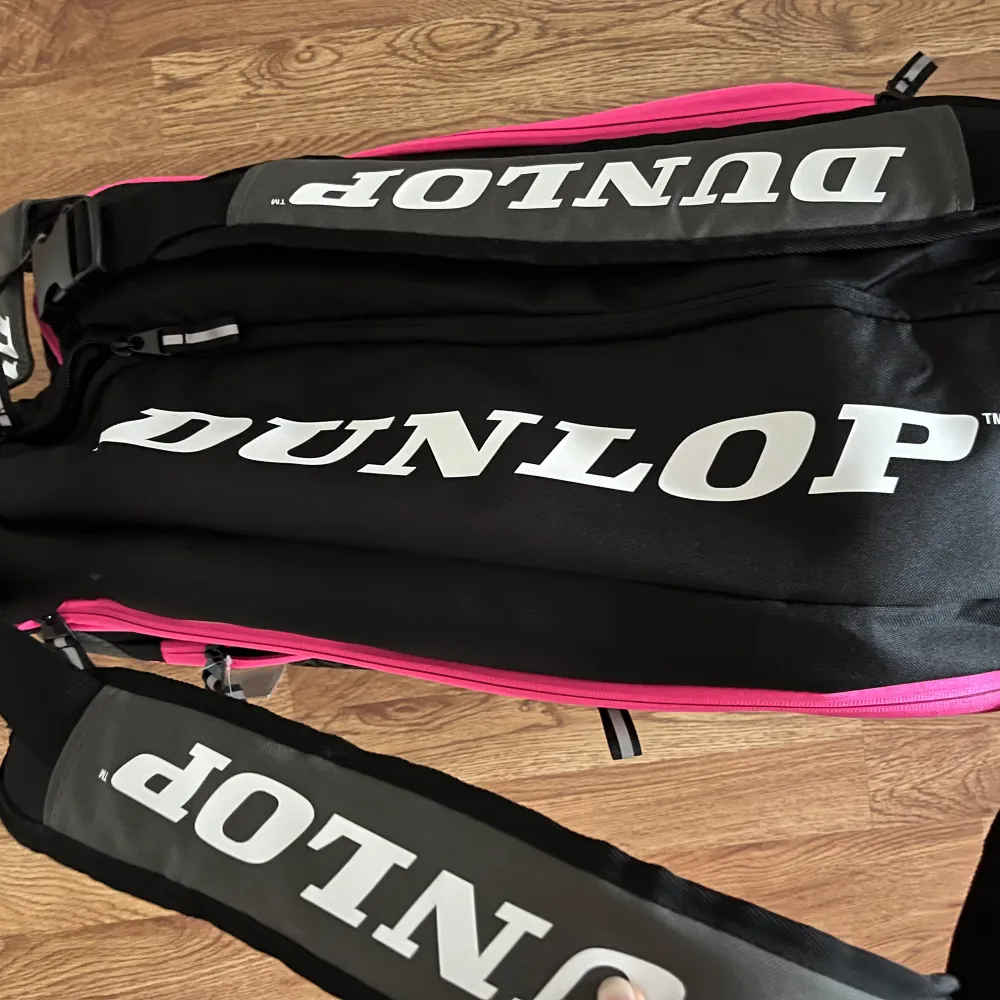 DUNLOP ELITE PINK THERMOBAG padel väska sälje. Ny, oanvänd, men lapp kvar. Svart/rosa.  Gott om plats och samtidigt stilig väska. Tre stora fack för rack och ett separat skofack (dvs separat från kläderna). Termoisolerad. Robust. Bekväma vadderade ha. Väskor.