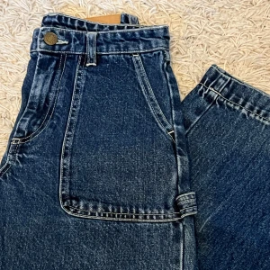 Blå vida jeans - Gulliga blåa jeans från Monki i bra skick! Storlek 24 i midjemått! Modell - lite kortare vida jeans, en detalj på vänster byxben! Pris 139 + frakt