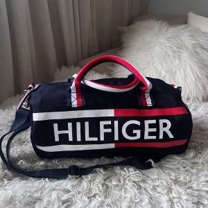 Väska, Tommy Hilfiger (ÄKTA) - Unik rymlig väska i nyskick! Har fack på insidan och stängs med en dragkedja. Både band för axelremsväska och för handväska, axelbandet är avtagbart.  Köpt i USA på Tommy Hilfiger butiken.