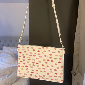 Väska pussmun - Väska från Carin Wester med pussmunnar på. Inga defekter eller skador. Långt justerbart band. Flera fack inuti. Säljer för 199kr❤️