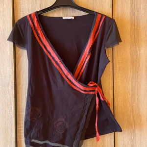 Crossover topp - Mörkbrun crossover topp med röda detaljer som man knyter på sidan. Toppen är i nyskick förutom snöret som är lite slitet✨står ingen storlek men sitter som S-M