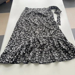 Sommarkjol - Längre kjol svart med små vita blommor. Kjolen går en bit nedanför knäna. Liten volang nertill som är snedklippt, mycket fin sommarkjol. 