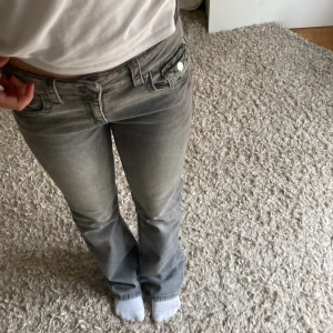Grå jeansbyxor från Gina Tricot - Nyskick! Ett par grå jeansbyxor från Gina Tricot i storlek 164. Byxorna har en bootcut-stil och är lågmidjade. De har fickor fram och bak samt knappar och dragkedja i gylfen. Pris går att diskutera!