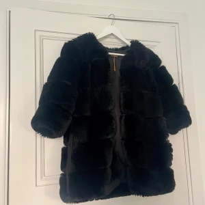 Faux jacka - Svart jacka passar bra för vinter/ kall höst. 3/4 ärmar Slutar strax ovanför knäna.  Kan stängas med hjälpa av hakarna (se bild) 