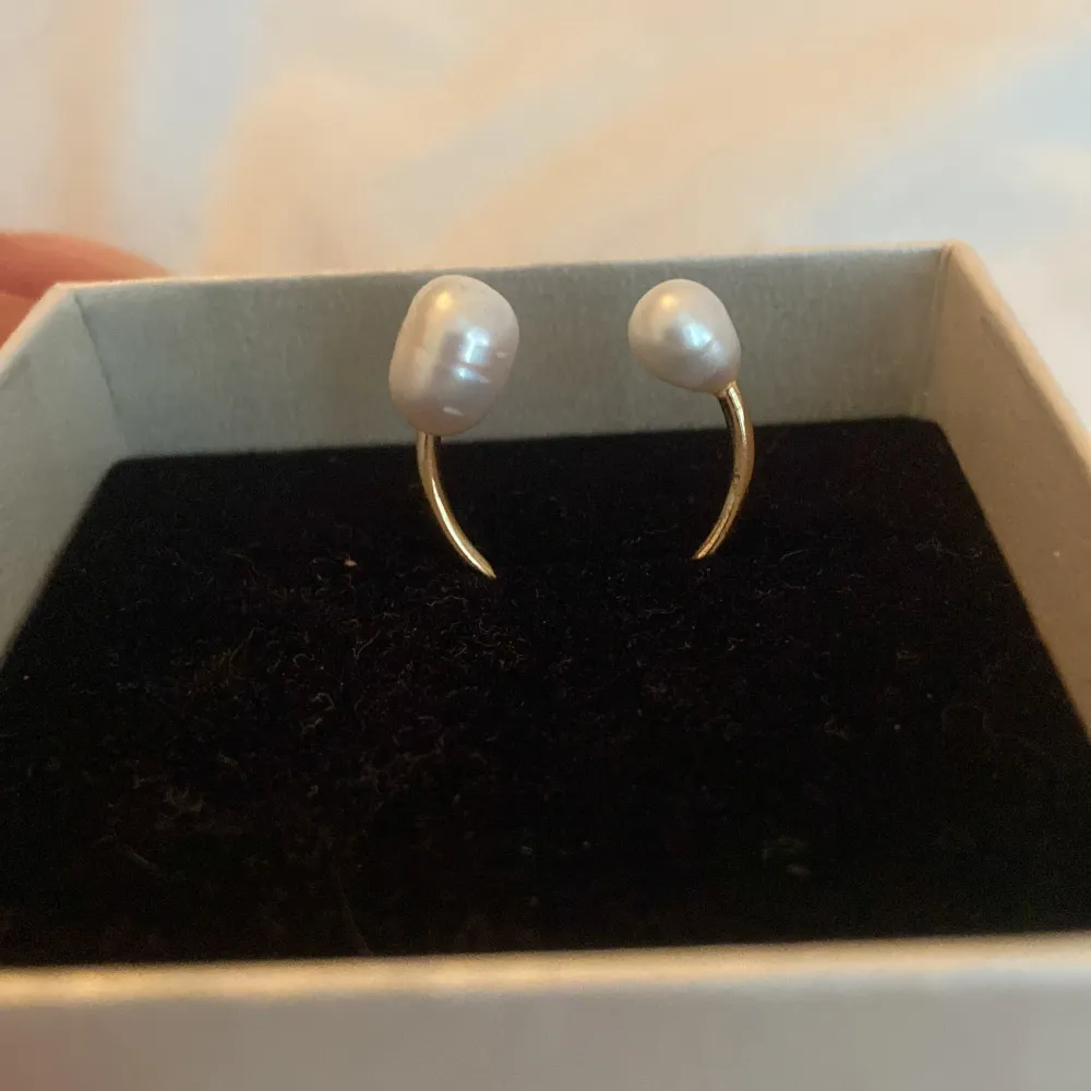 En elegant guldring med två vita pärlor. Ringen har en öppen design med en pärla i vardera ände.. Asusteet.