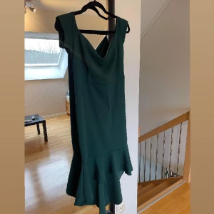 Mörkgrön klänning med volang - Mörkgrön maxiklänning med fina volanger ned till. Endast använd en gång. Storlek 44. Kan användas som off shoulder men även ha på axlarna. 