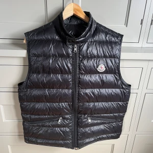 Moncler väst gui night blue - Västen är köpt på NK nyligen men säljer för den ej kommer till användning, knappt använd och är i 9/10 skick. Västen sitter lite kort på mig som är 187 cm lång. Är redo att gå ner i pris vid snabb och enkel affär.