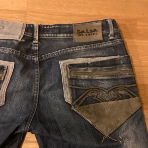Unika jeans med skin detaljer - 86cm i midjan, 91 cm i längden(jag har sytt upp dem) utsvängda och lågmidjade med unika detaljer av skinn, ned knapp