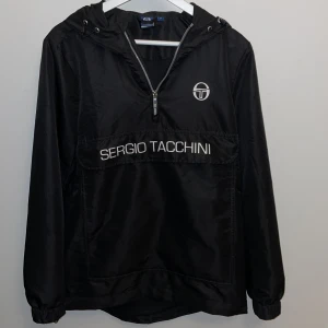 Sergio Tacchini jacka - Sergio Tacchini vindjacka i svart. Den är i bra skick och har inga hål eller defekter!