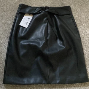 Skinnkjol från NA-KD  - Snygg skinnkjol ifrån NA-KD säljer jag på grund av att den är lite för tajt för mig:/ prislapp sitter kvar och den är aldrig använd! Snygg detalj i midjan också! Köpt för 400kr men säljer för 300kr!