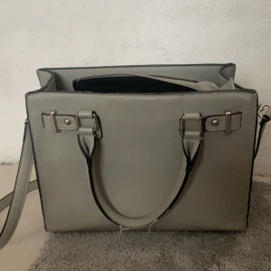 Grå väska  - En väska som har används mycket men är i bra skick. Man får plats med många saker och man kan bära väskan på två olika sätt🩷