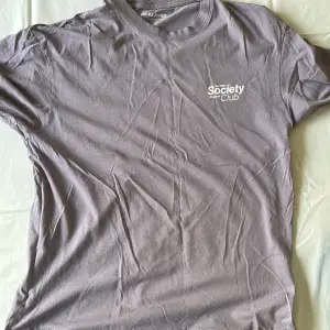 En lila t-shirt med Society originals club tryck på vänster bröst