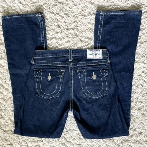 Lågmidjade bootcut True Religion jeans - Säljer mina True Religion jeans då de är smått för små för mig. ❤️ De har en lågmidjad och bootcut modell, med vita stygn. Vet ej i vilket format storleken är i men innerbenslängden är 79cm och midjemåttet 36cm. Köpare står för frakt! 💞