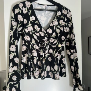 Svart blus - Svart blus med blommor på. Formar sig runt bysten super fint!  Storlek S Plagget finns på fler sidor så kan säljas. 