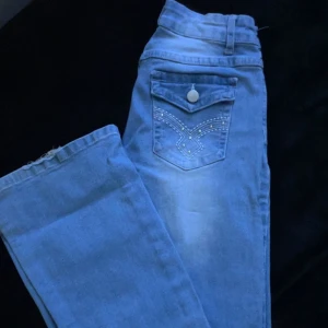 Blå jeans med detaljer på fickorna  - Jättefina fickor på byxorna, lågmidjade. Lite trådar har åkt av på slutat av jeansen därför blir de lite billigare. 