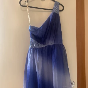 Blå klänning  - Den blå klänningen har bara en arm och en stulen gul "arm" för upphängning. Den är tajt vid brösten för att hålla upp klänningen och har en snedskuren längd, kort till höger och längre till vänster. Klänningen är ny o vacker och har en diamantdekoration. 