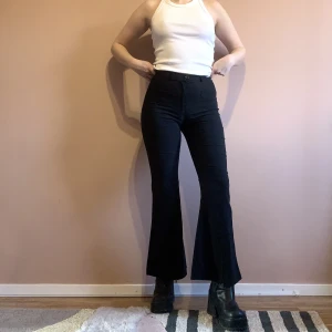 Svarta 90s grunge byxor - Svarta högmidjade byxor med grunge-vibe. Utsvängda ben med dragkedjor. 2hand och väl använda av mig men i gott skick. Lappen är borta men bedömer dem vara strl 36. Midjemått 68, längd mätt från innerben 75 cm. Stretchigt material, bekväma.